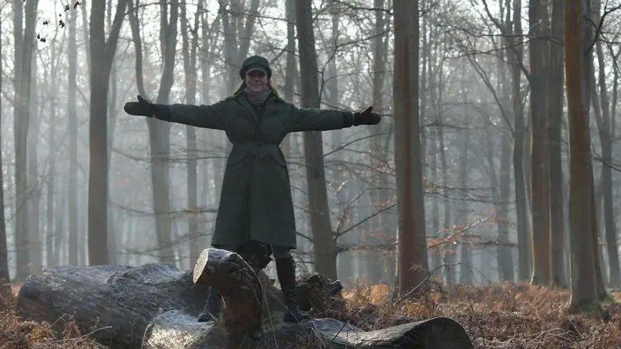 Catherine Princess of Wales, with her arms open, wearing a winter coat, in woodland in Windsor