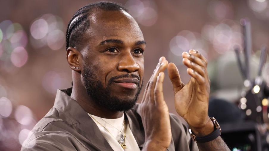 Michail Antonio applauds West Ham's fans, wearing a grey shirt over a white T-shirt, surrounded by bubbles 