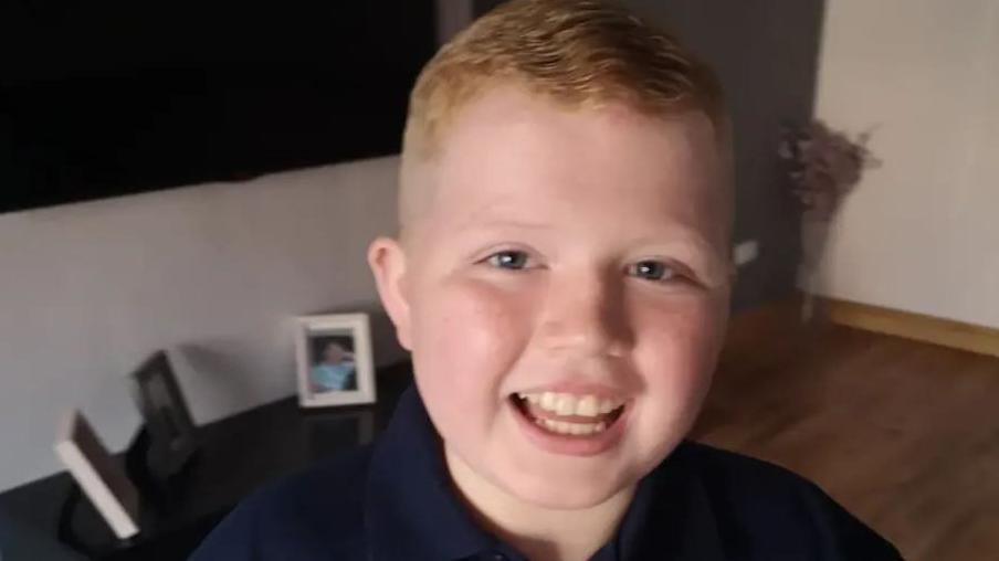 A young boy with ginger hair smiles towards the camera 