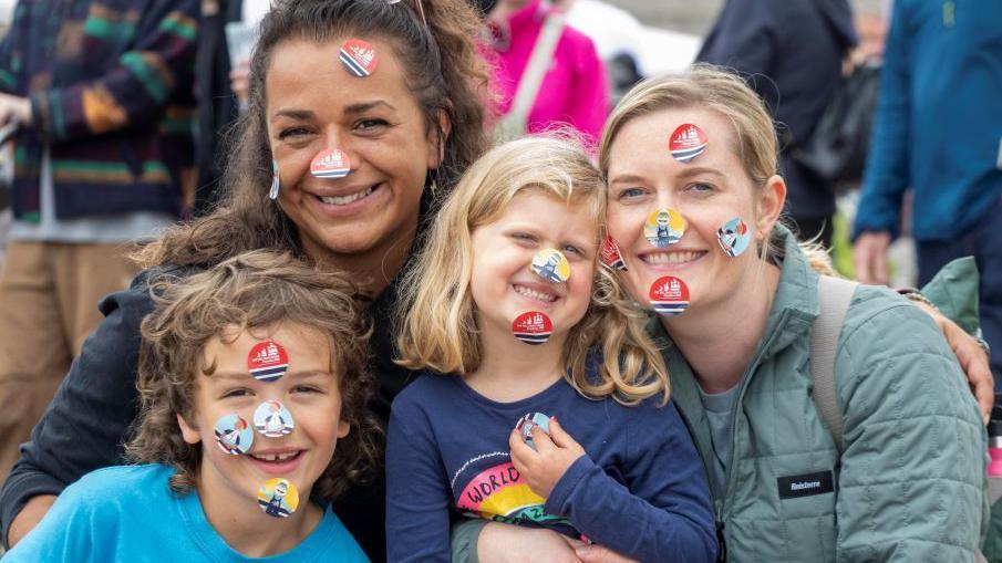 Two women and young children with tall ships stickers on their faces.