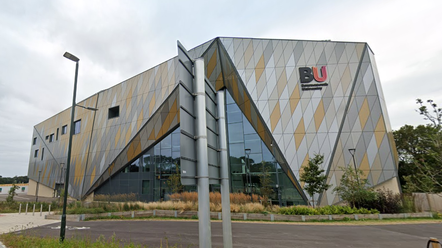 Building on Bournemouth University campus, which has an angular design with silver and gold panelling. A pink and black 'BU' logo is on the side of the building.