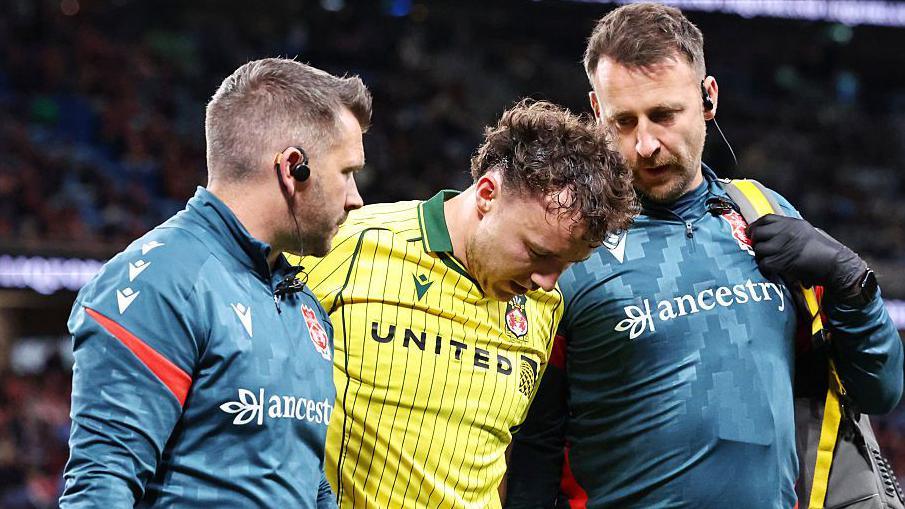 Ollie Rathbone successful a yellowish Wrexham garment being supported stepping disconnected nan transportation by 2 Wrexham backroom officials