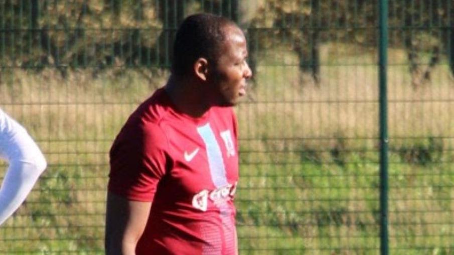 A man wearing a red football top stands on a field looking away from the camera.