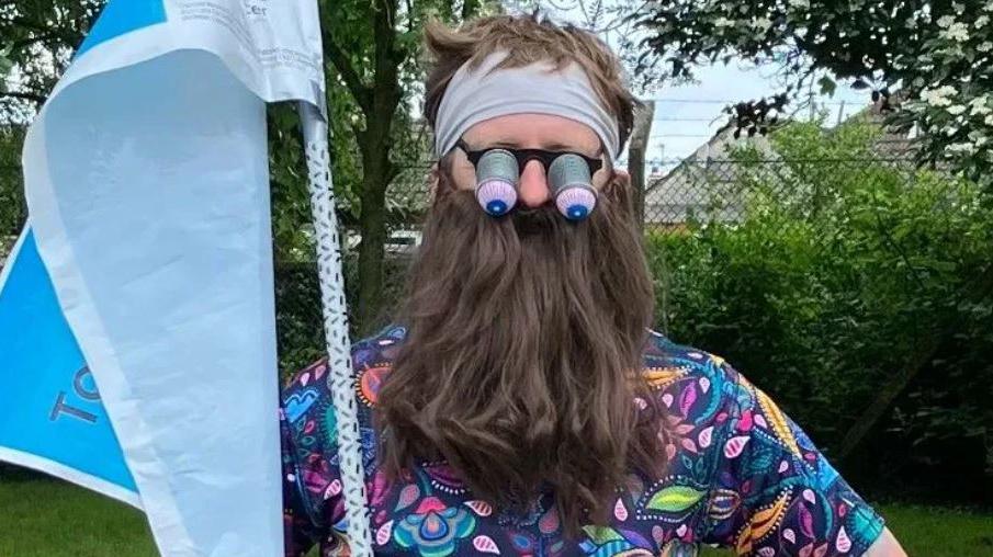 Man with false beard holding a flag wearing springy eye goggless and a fake beard