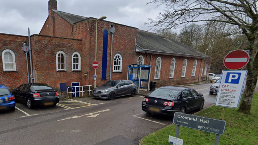 The Crosfield Hall is a brick building with a high, single storey and arched windows. It is surrounded by a surface car park.