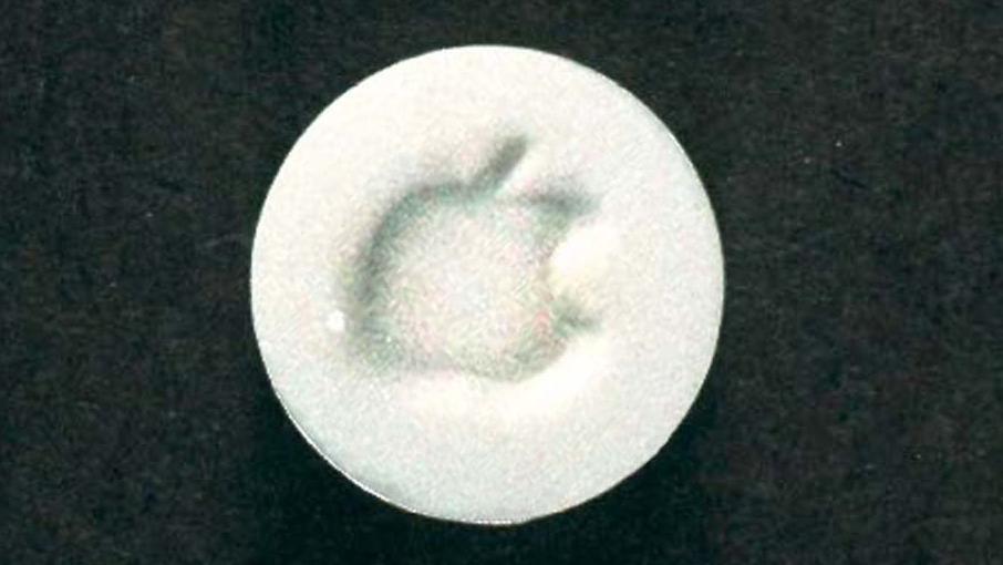 A grainy picture of a white circular tablet with an image of an apple imprinted onto it.