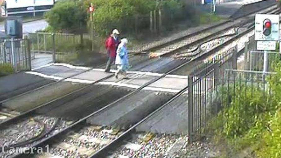 An older couple walk across Wareham crossing on 12.5.09, before barriers were installed. A red light is showing on one side of the crossing.