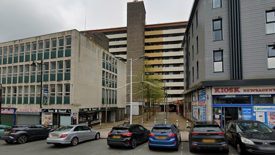 Flat blocks and shops in central Pontefract. There are cars parked outside the buildings.