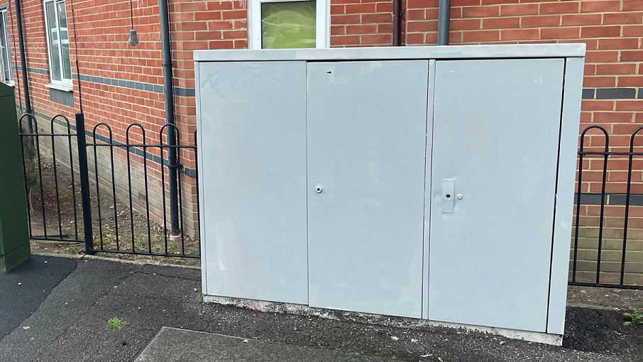 A grey utility box box in front of homes which has been painted over with grey paint.