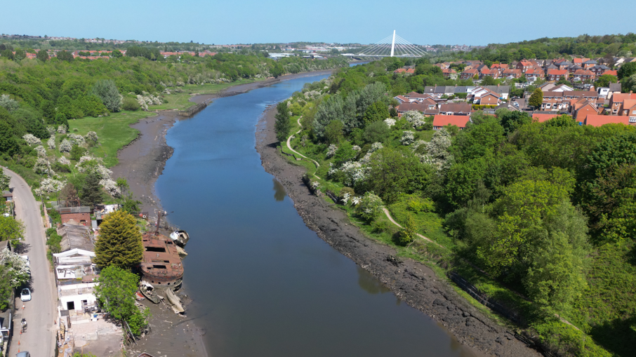 A drone photograph of the River Wear between North and South Hylton, where the stones have been located. The Shipwrights pub, which is a white building, is on the north bank, on the left. There is a housing estate on the other side of the river. The Northern Spire bridge is visible in the distance. 