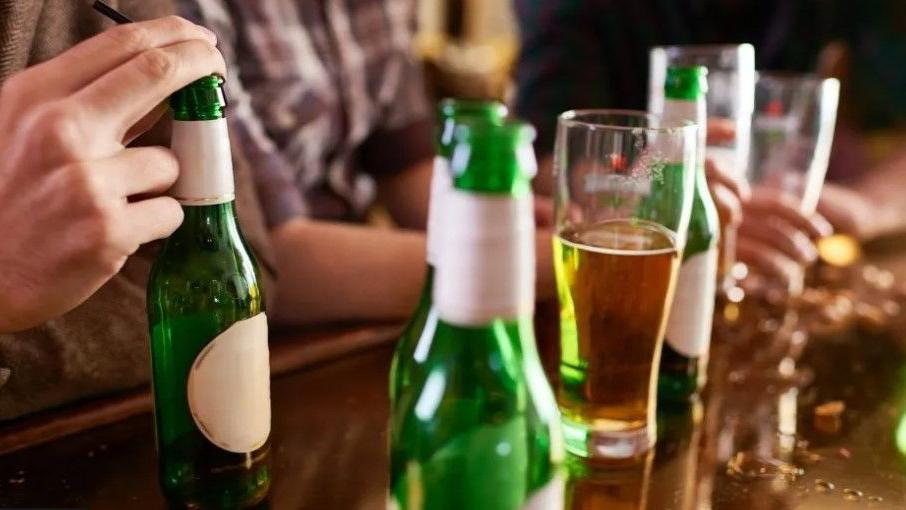 A man 's hand on a bottle of beer, with bottes and a pint on a table