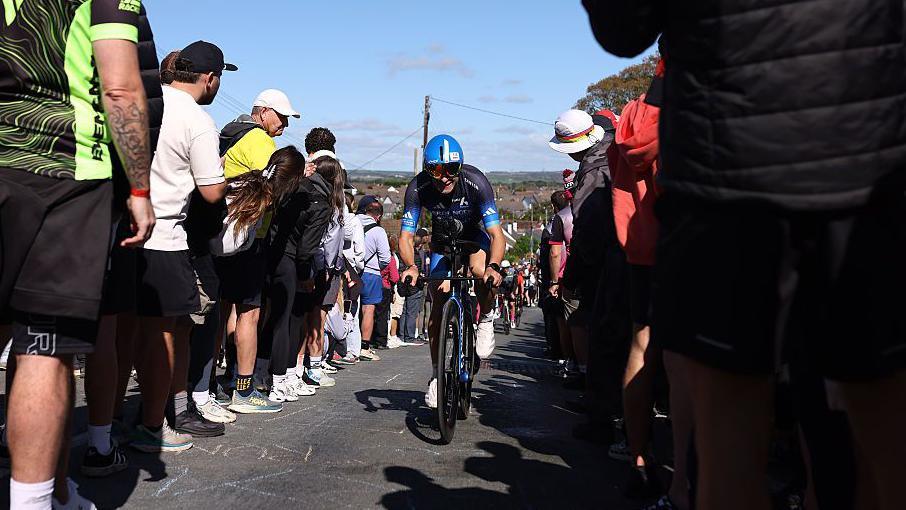 A cyclist wears a black top and blue helmet as he passes between crowds of people