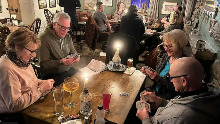 A group of people playing cards and drinking at a pub table 