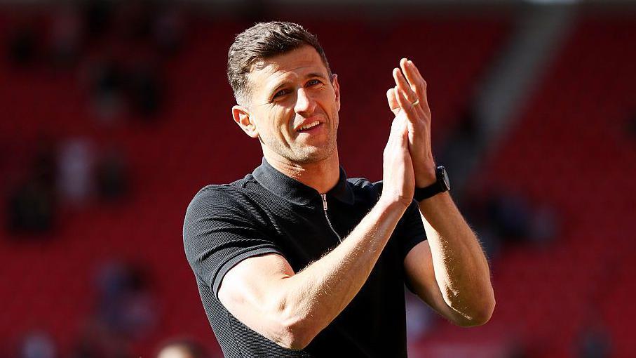 Portsmouth boss John Mousinho wearing a black short sleeved top applauding supporters after a win at Middlesbrough