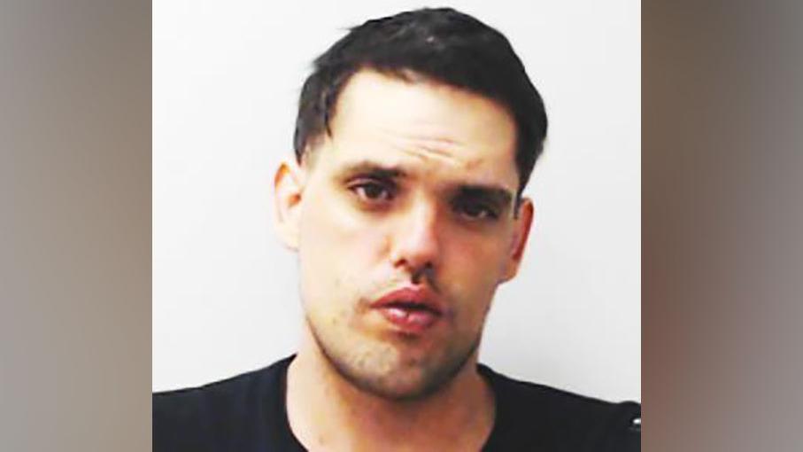 Man with dark hair and dark top looking at camera in police mugshot