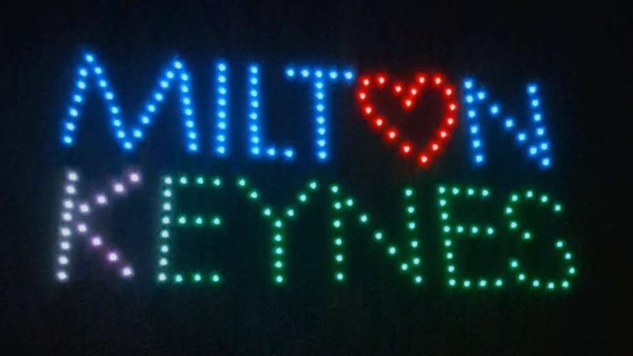 Milton Keynes spelt out by drones, showing different colours and the O in Milton is a red heart. The sky behind is black. 
