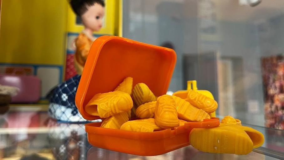 A pile of small yellow dolls shoes spilling out of a mini orange suitcase