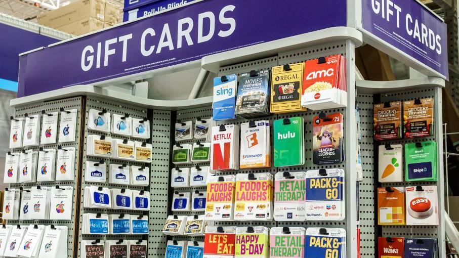 A stand containing hundreds of multi-coloured gift cards, showing various brands. A purple sign with white writing says GIFT CARDS.
