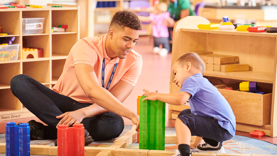 Stock image of a primary teacher and a young child playing with Lego in a nursery or young school setting. 