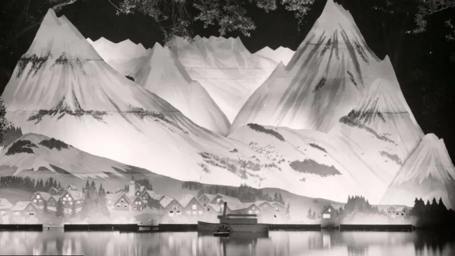 A black and white photo of an Alpine scene with peaks lit up behind small houses