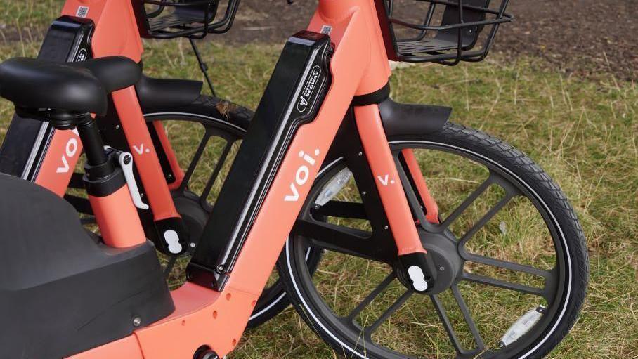 Close up of a red Voi electric bike with grass in the background