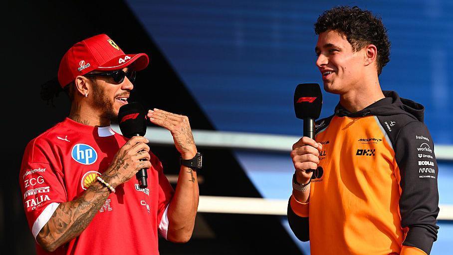 Ferrari's Lewis Hamilton and McLaren's Lando Norris speak to each other while holding microphones on stage at the Qatar Grand Prix