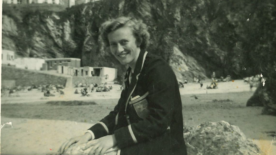 Mary on a beach, wearing a smart blazer and smiling at the camera. 
