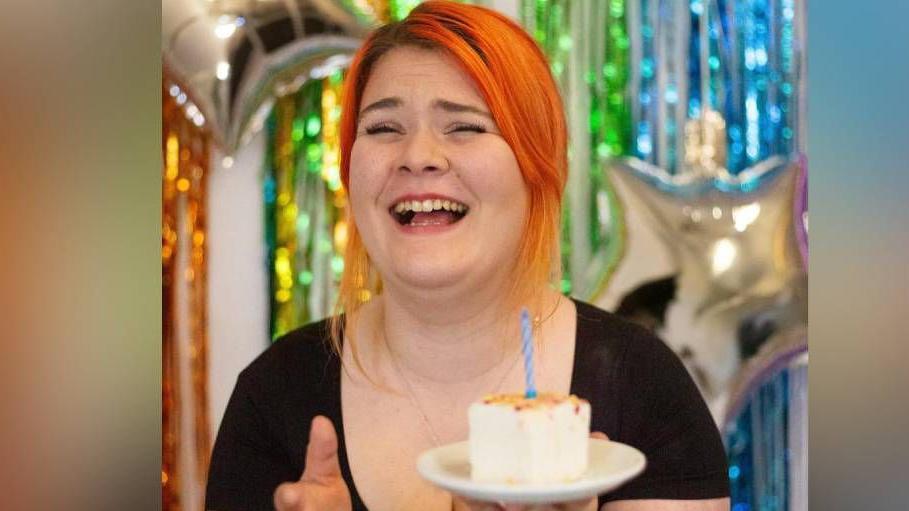 Emily Roberts smiles as she holds one of her homemade marshmallows in front of balloons