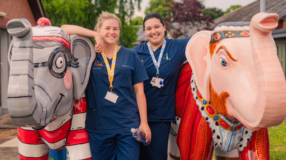 Two St Giles Hospice workers flanked by two elephant sculptures, one painted like Where's Wally?