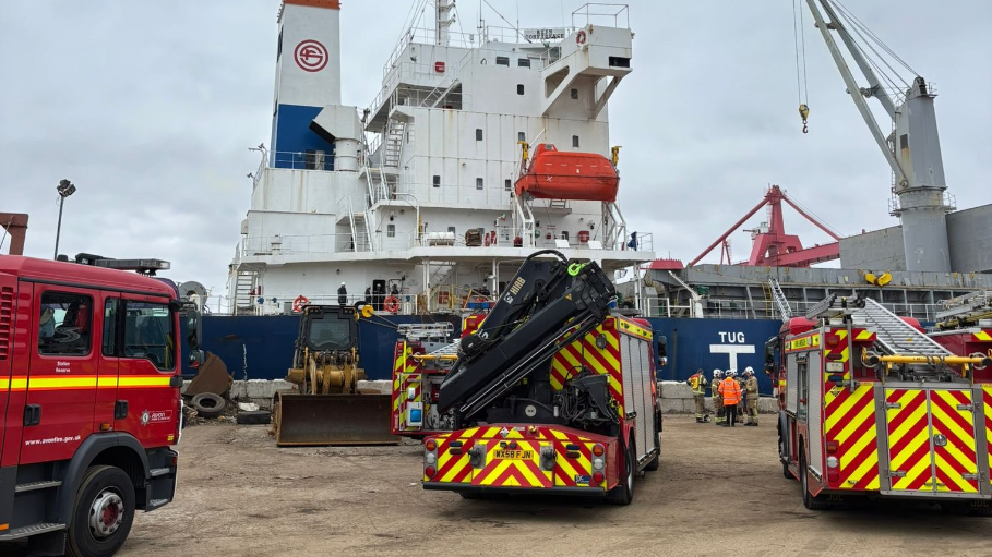 Three fire engines facing a large white ship. 