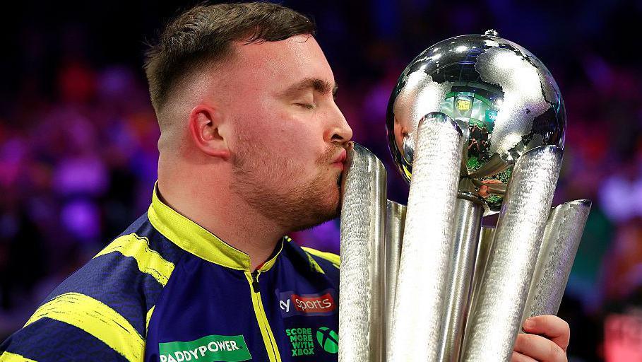 Luke Littler celebrates with the trophy after retaining his world darts title in 2026