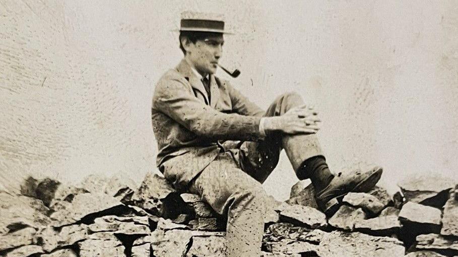 Photograph of the Cheshire mountaineer George Mallory. The black and white image shows him sitting on a dry stone wall.