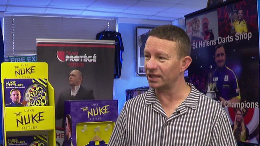 Karl Holden in his shop, surrounded by images of Luke Littler