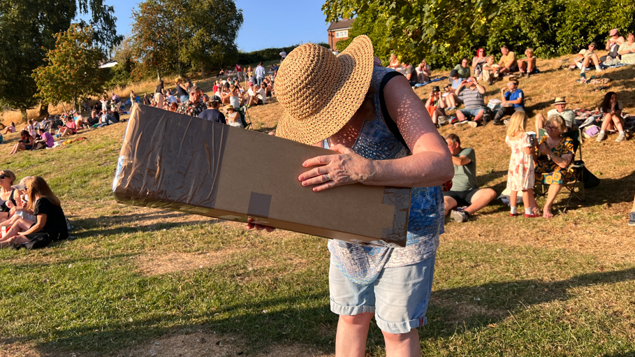 A woman is looking through a hole in a giant cardboard box at the sun