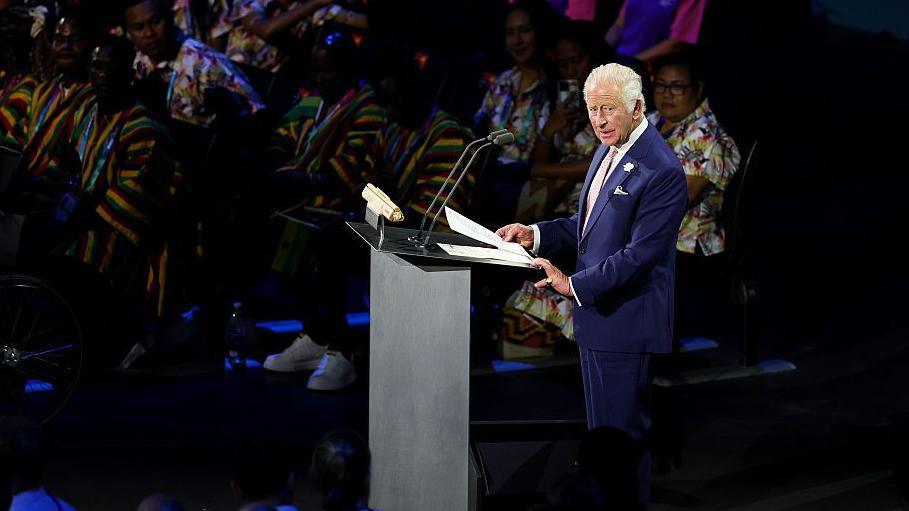 King Charles, in a blue suit, gives a speech from behind a lectern during the Commonwealth Games opening ceremony
