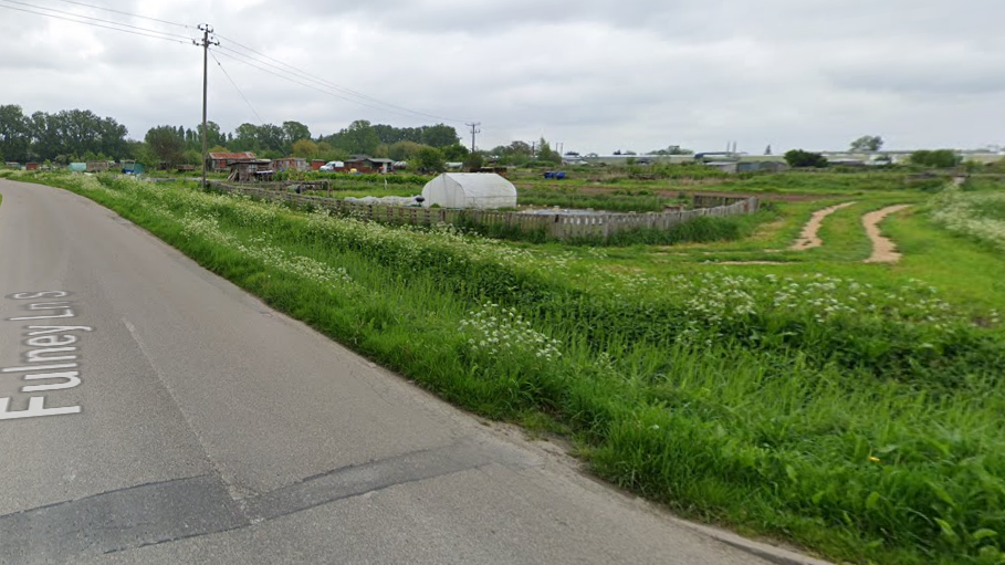 Allotments with sheds and greenhouses are next to Fulney Lane, a dirt road runs off to the right of the photograph. 