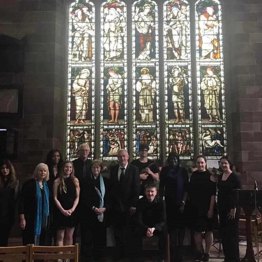 A group of people in black suits and dresses stand in front of the stained glass window in a church