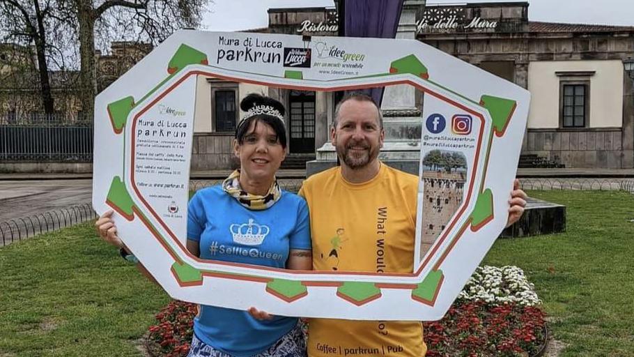 A woman in a blue running T shirt and a man in a yellow running T shirt pose behind a cardboard frame