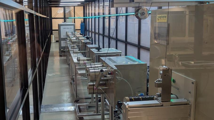 A row of metal machines inside a glass-panelled hallway used in the production of graphene products. 