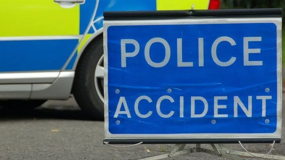 A blue and white police signboard in front of a police car - parked on the road.