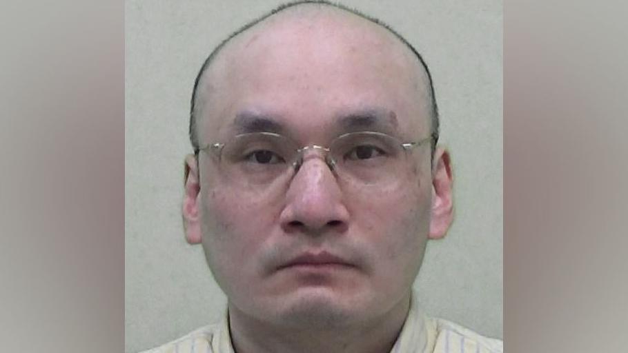 Mugshot of Thomas Kwan, he is bald and wearing glasses and a yellow shirt with blue pinstripes.