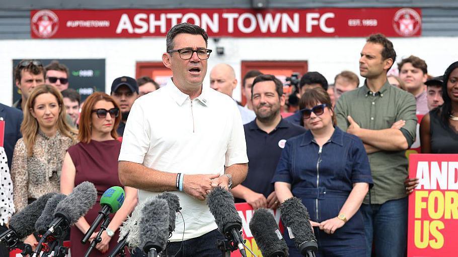 Andy Burnham speaks in front of a sign which reads Ashton Town Football Club