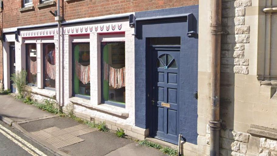 Google street view of 11 Lansdown in Stroud, Gloucestershire. A blue door can be seen, with a number 11 on it. There are four large windows next to the door. 