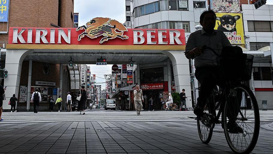 A man riding a bicycle, with a building behind him that reads: Kirin Beer