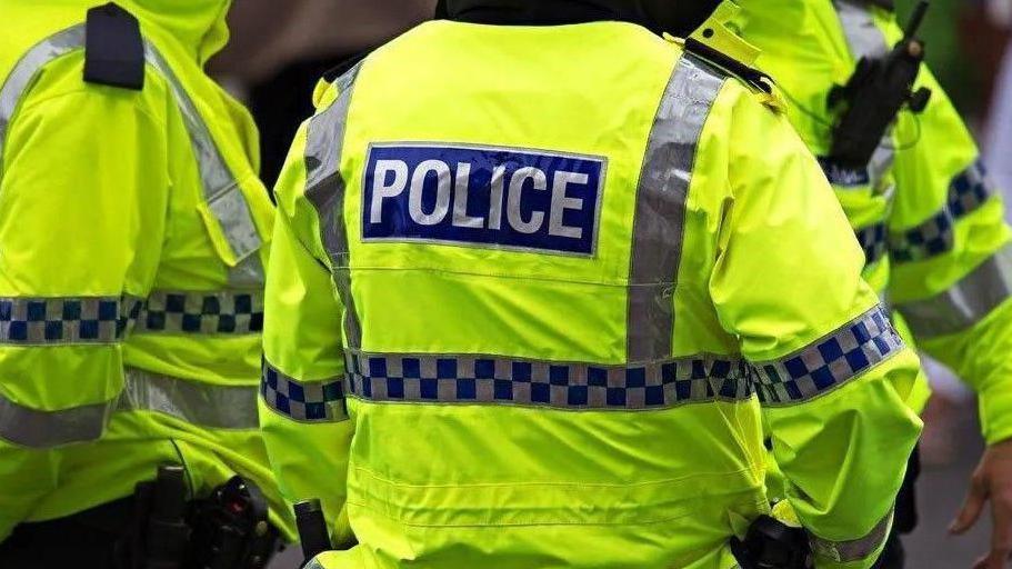 A picture of three people wearing high visbility yellow jackets with the word police written on the back. 