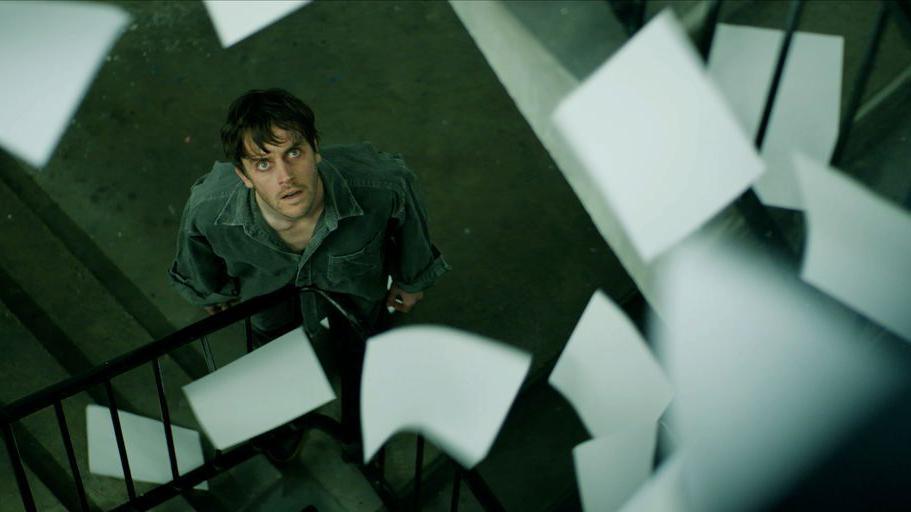 A man looks up at sheets of paper falling from above.