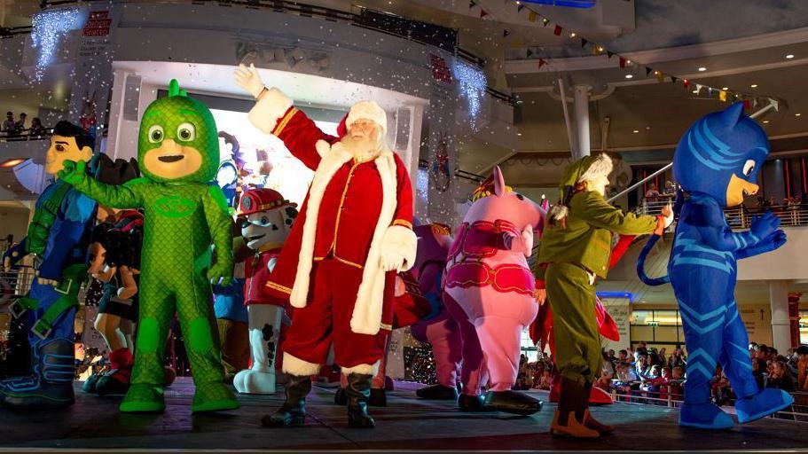 Father Christmas along with other children's favourite characters such as PJ Masks waves to the crowd of child from the stage during Trafford Centre's Christmas Parade.