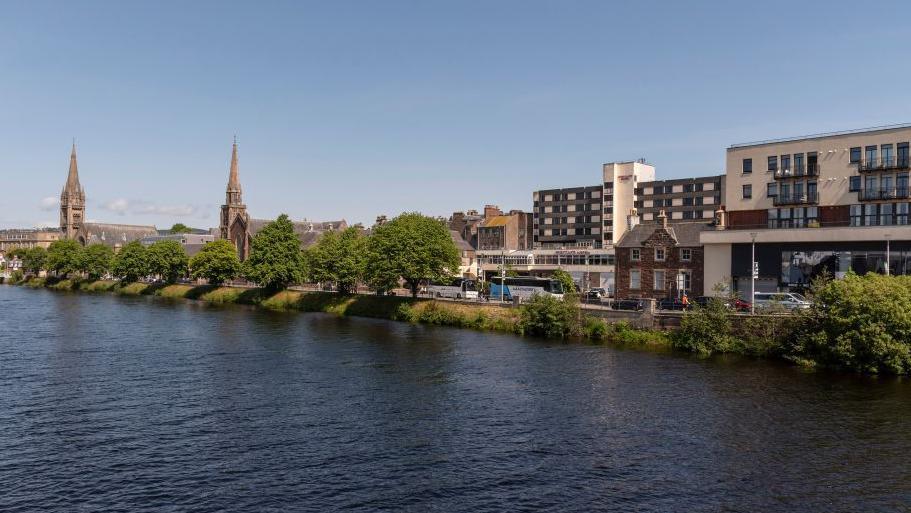 The River Ness flows through Inverness. There are two spires on the bank.