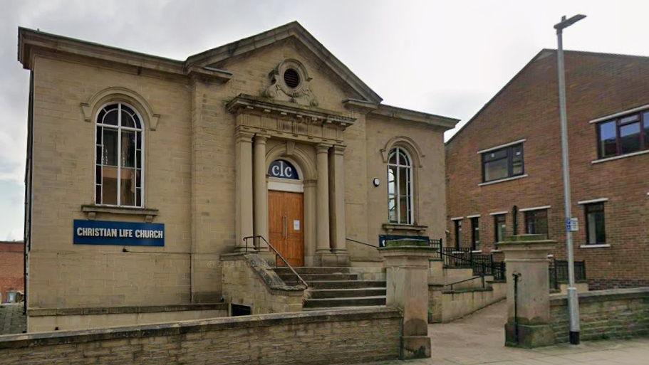 The front of a beige-coloured Georgian building with oak front doors. A sign saying 'Christian Life Church' is to the left of the doors.