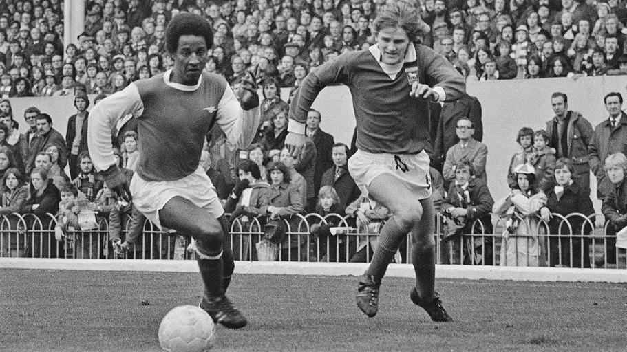 A black and white picture of Arsenal player Brendon Batson sprinting for the ball in a race against an Ipswich Town player at Highbury in 1973